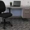 Office workspace featuring a Black Fabric Task Chair W/ Adjustable Arms, a desk with a laptop and a small plant, set against a carpeted floor.