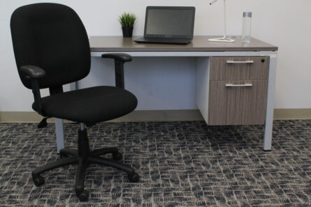 Office workspace featuring a Black Fabric Task Chair W/ Adjustable Arms, a desk with a laptop and a small plant, set against a carpeted floor.