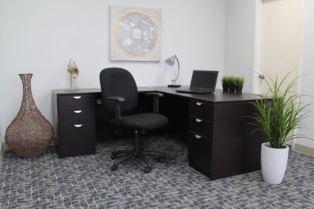 A modern office with a dark wood desk, Black Fabric Task Chair W/ Adjustable Arms, laptop, decorative vases, and green potted plants, under soft lighting.