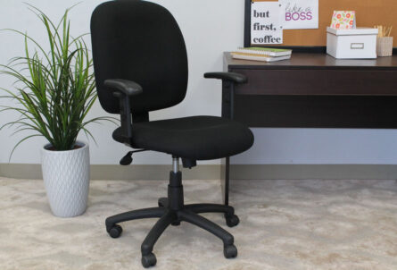 A Black Fabric Task Chair with Adjustable Arms in front of a desk with a plant, books, and a coffee mug.