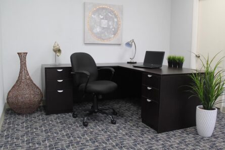 A modern office space featuring a desk with a laptop and TOS Heavy Duty Task Chair, flanked by decorative vases and plants, under a wall-mounted abstract art piece.