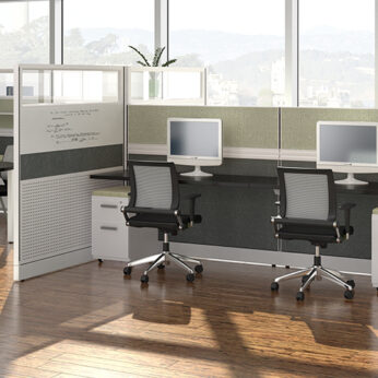 Modern office interior featuring two cubicles with computer monitors, ergonomic chairs, and a panoramic view of a lake through large windows.