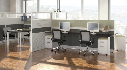 Modern office interior featuring two cubicles with computer monitors, ergonomic chairs, and a panoramic view of a lake through large windows.