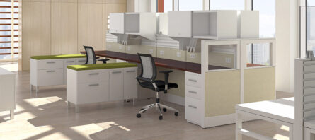 Interra Series office space with cubicles, featuring white storage cabinets, black chairs, and wood-topped desks in a bright room with large windows.