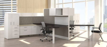 Modern office interior with Interra Series desks, chairs, and storage units in a bright room with large windows overlooking a city.