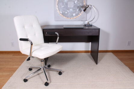 A modern home office setup featuring a Modern Office Chair w/Chrome Arms- White and a dark wooden desk with a metallic desk lamp, placed on a beige rug.