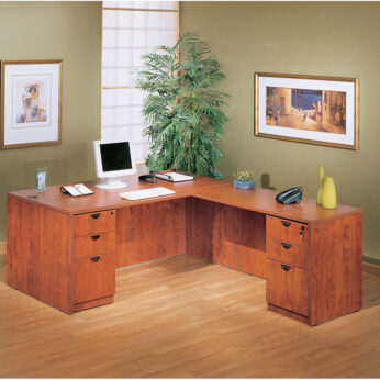 Sentence with replaced product: A 71 Inch Executive L-Shape Corner Desk with Dual File Storage Pedestals, computer, notepad, telephone, and decorative plant, situated in a room with framed artwork and a potted plant.