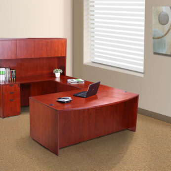 Modern office setup with an Executive U-Shaped Curved Bow Desk with File Storage Pedestal and Hutch, Cherry, laptop, and shelving unit in a room with beige walls and a window with blinds.