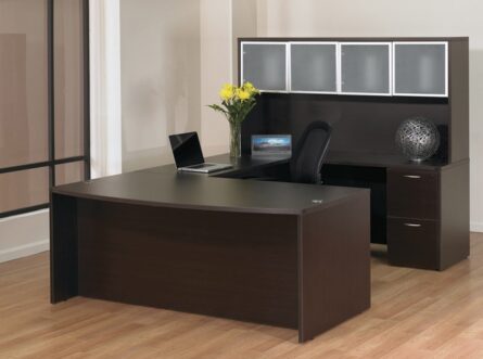 Modern office setup with a dark wooden desk, chair, laptop, and decorative items in a room with a large window and light flooring.