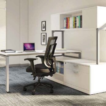 Modern office setup with a Elements Workstation Desk #1, ergonomic black chair, laptop, and a white shelf with books in a well-lit room.