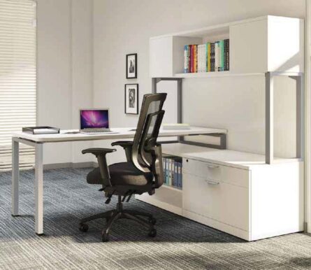 Modern office setup with a Elements Workstation Desk #1, ergonomic black chair, laptop, and a white shelf with books in a well-lit room.