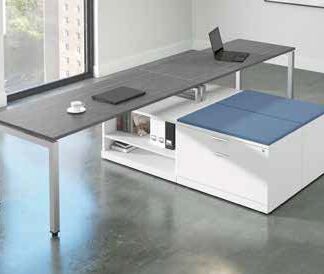 Modern office with an Elements Series L shaped desk without hutch and a multifunctional storage cube, featuring a laptop, cup and book, set against a window with a city view.