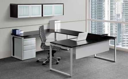 Modern office setup featuring a sleek Elements U shaped desk with a laptop, rolling chair, filing cabinet, and shelves, by a large window overlooking skyscrapers.