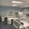 Empty office space with multiple TOS Quickship Cubicle Systems, white desks, and gray carpet flooring under fluorescent lighting.