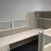 An empty TOS Quickship Cubicle System with white partitions and built-in shelves against a grey wall.