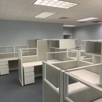 Empty office space with rows of unoccupied TOS Quickship Cubicle Systems and white desks under fluorescent lighting.