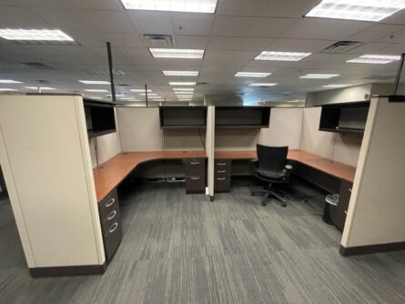 An empty office space with Haworth 67" tall cubicles, chairs, and partition walls under fluorescent lighting.