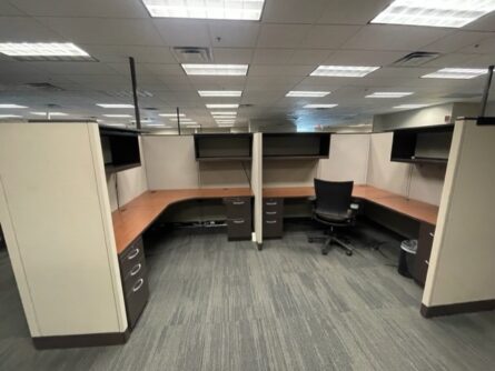 A cubicle with two desks and a chair.