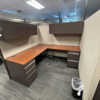 Haworth 67" tall cubicles with two empty desks, overhead cabinets, and a small trash can, set in a carpeted office area.