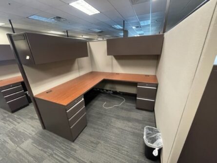 Haworth 67" tall cubicles with two empty desks, overhead cabinets, and a small trash can, set in a carpeted office area.