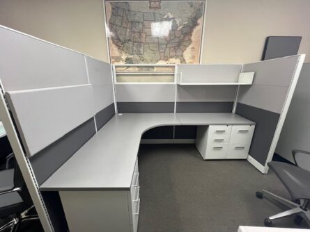 Friant Novo Series cubicle with a gray l-shaped desk, a wheeled chair, a white filing cabinet, and a world map hanging above.