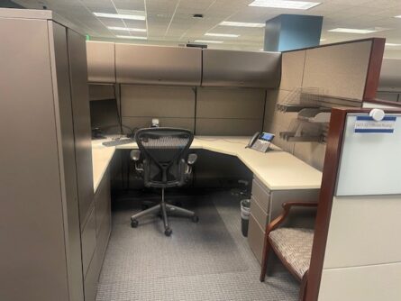 A cubicle office with a desk, chair, and filing cabinets.