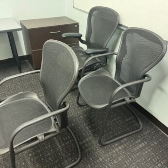 Three black mesh office chairs in a room.